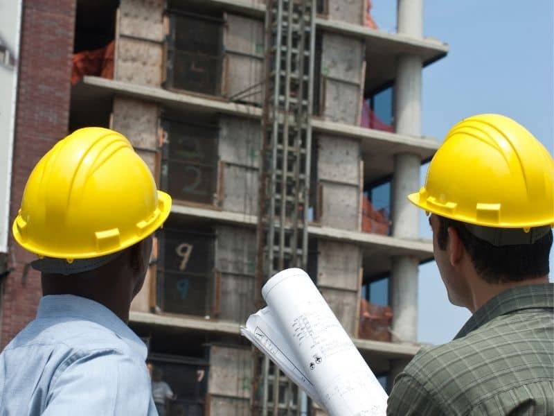 Construction professionals reviewing plans in front of a building project before survey layout and construction activities begin.